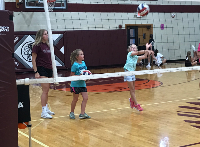 girls hitting volleyball over net